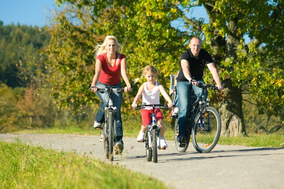 Casal e uma criança andando de bicicleta em parque 